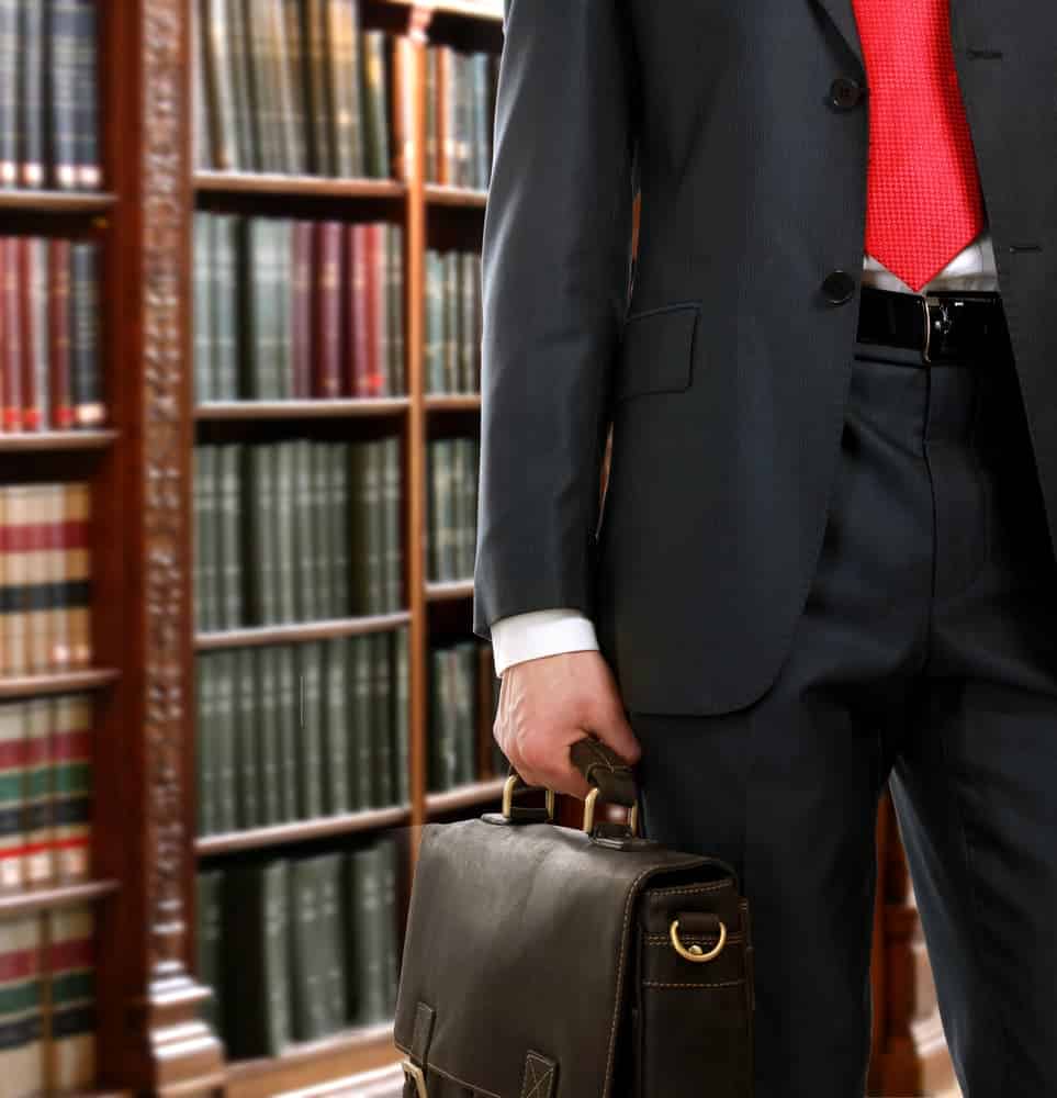 Closeup of a lawyer wearing a suit and holding a briefcase in a library.